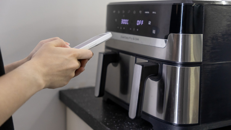 Person standing in front of air fryer, holding phone