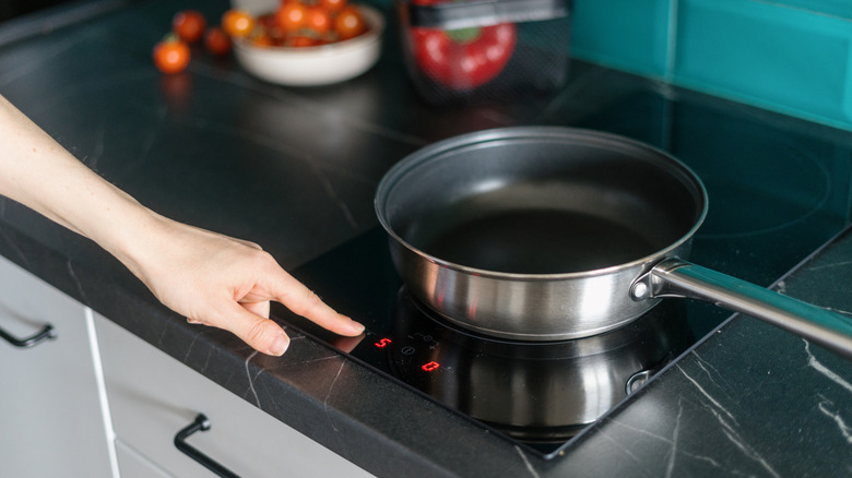 Person setting stove to high temperature, with pan on top