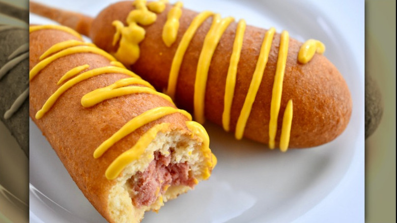 Close up of two corn dogs and mustard with a bite taken out of one