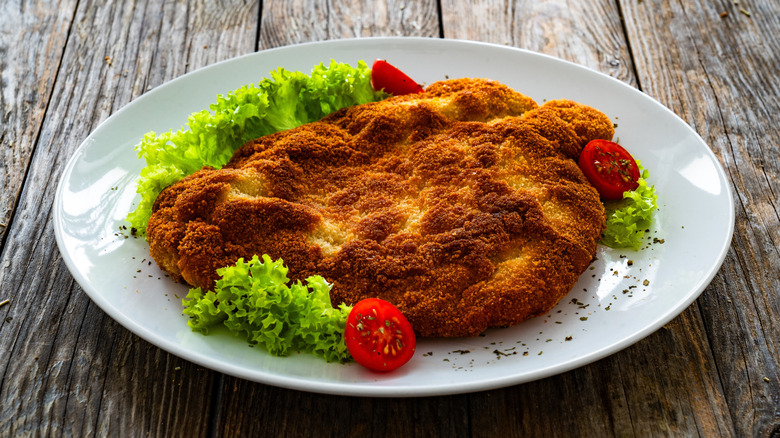 Crispy fried pork chop on a white plate with garnishes