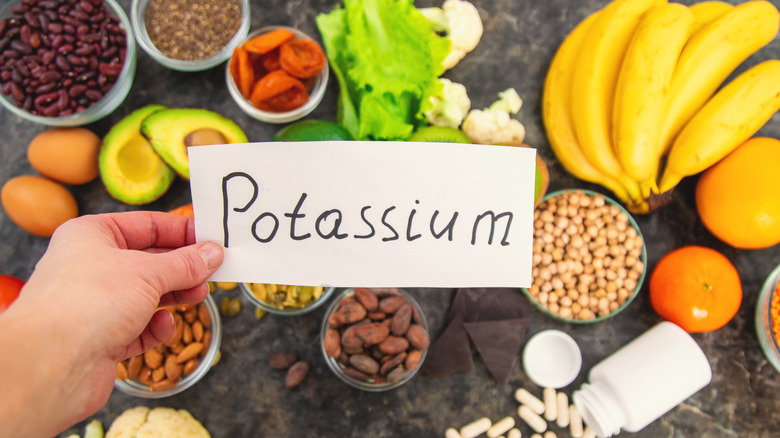 A selection of potassium-rich foods sit behind a sign saying "potassium," being held by someone's hand