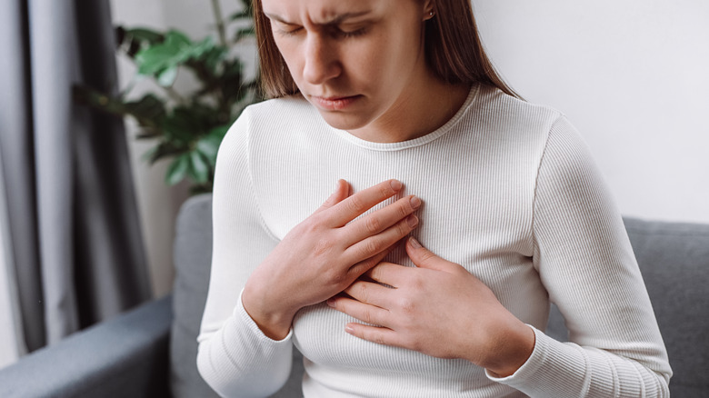 A young woman clutches her chest in pain from heartburn