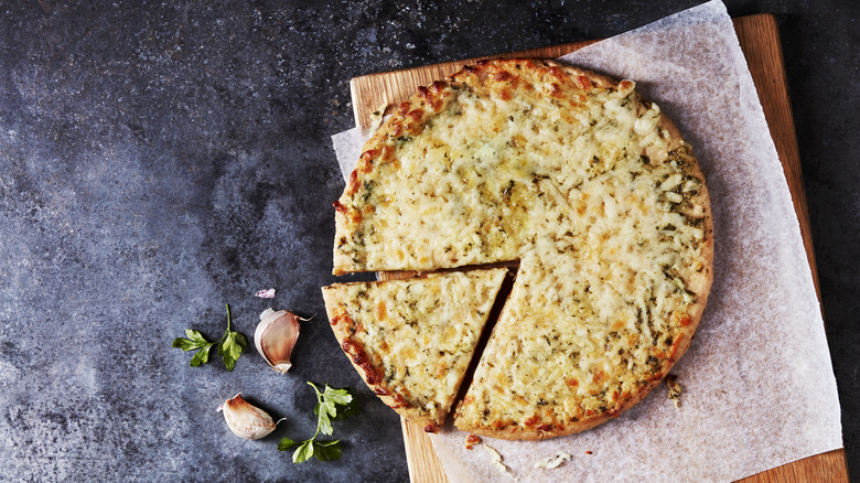 Cheese pizza, with garlic cloves sitting next to it