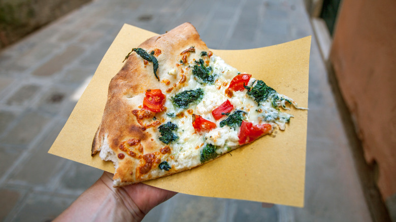 A slice of Neapolitan-style pizza being held on a napkin in an Italian street