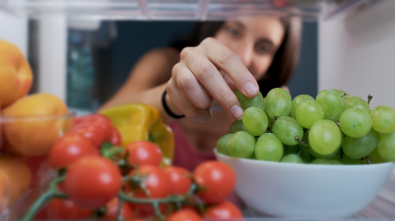 A woman reaches into a fridge and grabs a grape