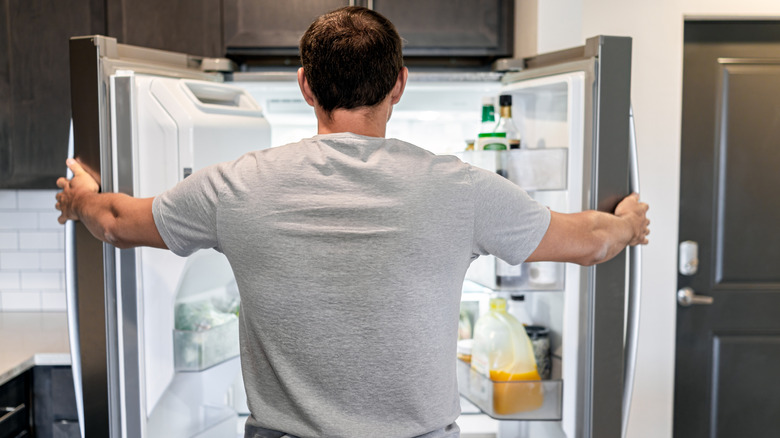A man looks into his fridge, viewed from the back