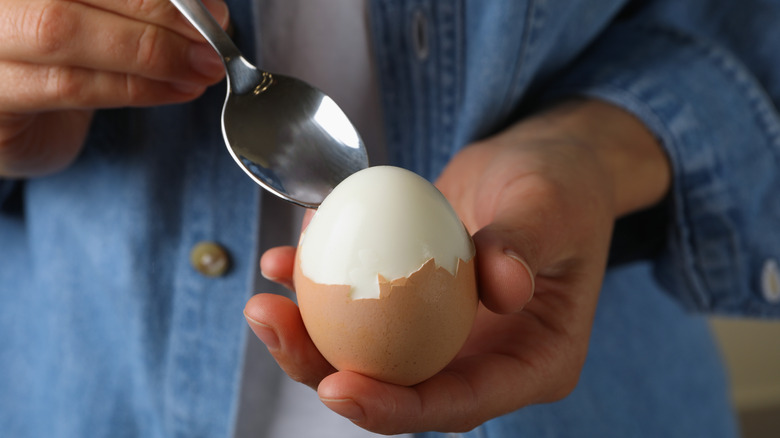 person peeling hard-boiled egg with spoon