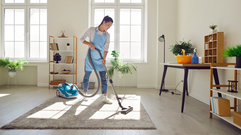 A woman in an apron vacuums her home