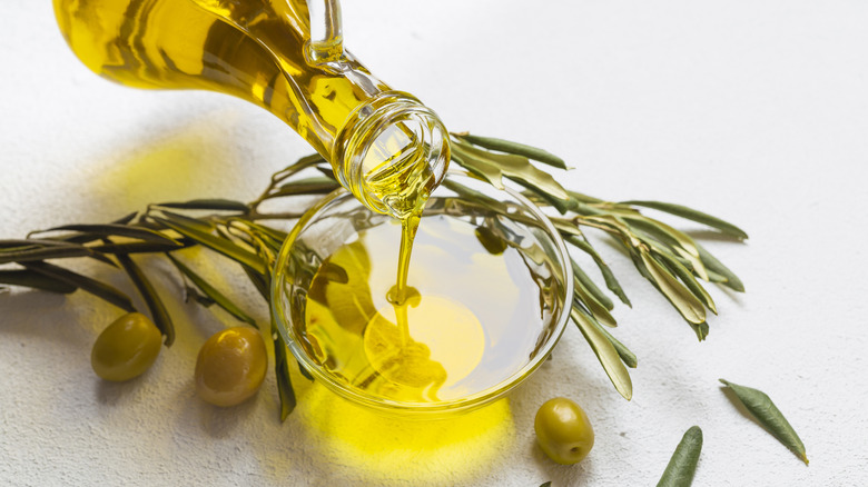 Olive oil being poured into a glass with fresh olive branch