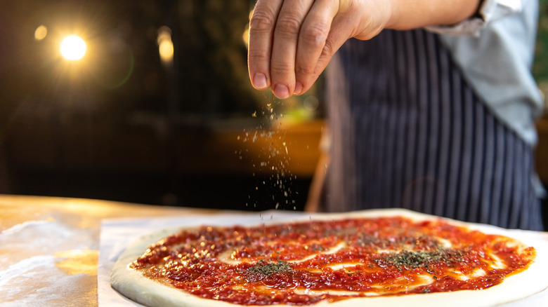 cook sprinkling herbs on pizza