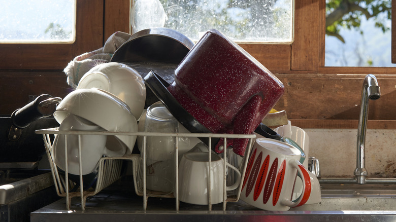An old dish drying rack filled with dishes in front of a window