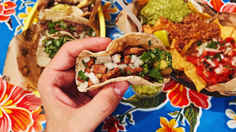 Overhead shot of a hand holding a taco, with Mexican dishes underneath