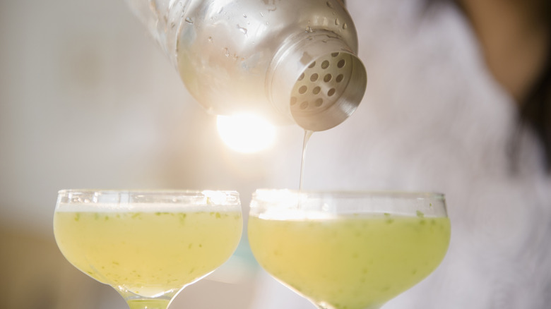 A bartender pours cocktails into two coupe glasses