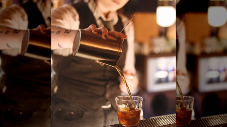 A bartender pours a cocktail into a glass