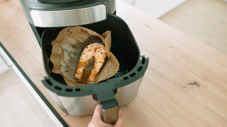 Person pulls a cooked salmon fillet out of an air fryer