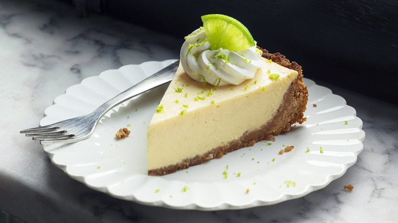 Slice of key lime pie on white plate with silver fork