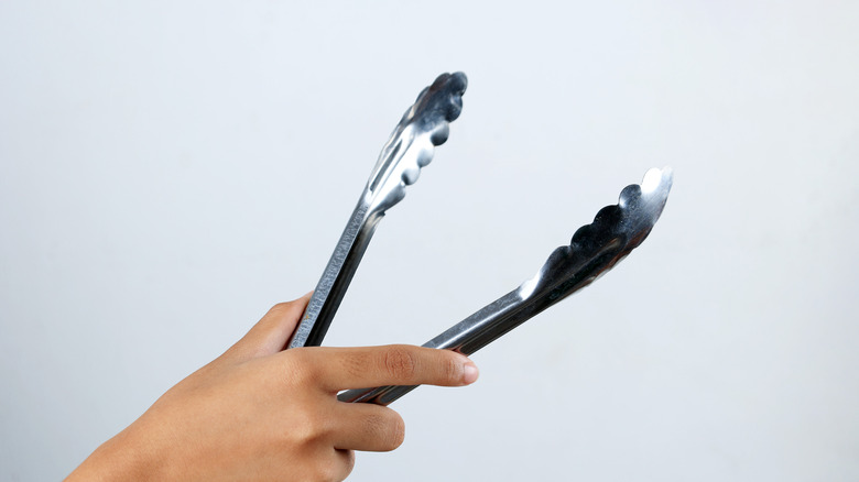 Hand holding stainless steel tongs