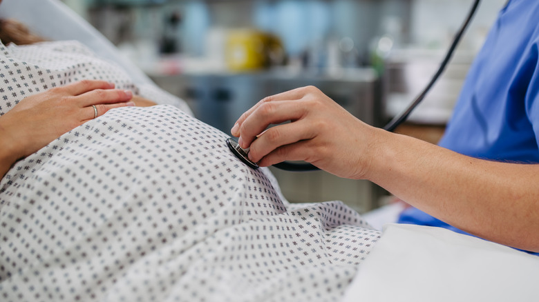 Doctor using stethoscope to listen to pregnant person's belly