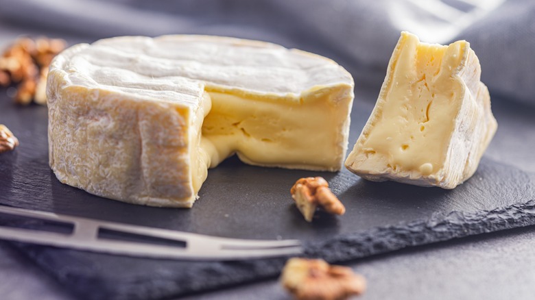 Brie with wedge sliced from it, with walnuts