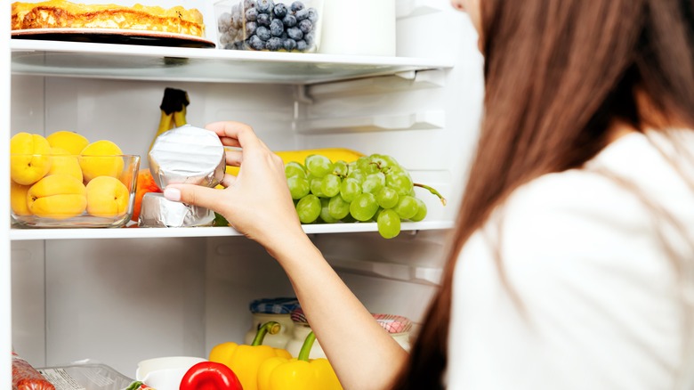 Woman taking wrapped brie out of fridge