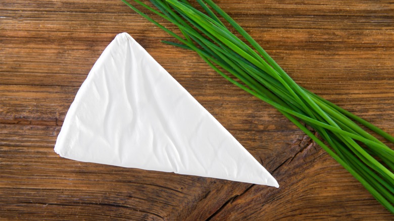 Wedge of wrapped brie with chives on wooden board