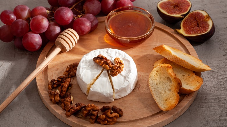 Brie on wooden charcuterie board, with fruits, bread, walnuts and honey