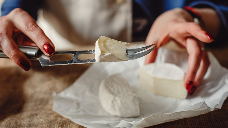 Woman cutting wedge of brie and displaying it on knife