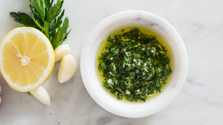 Small bowl of chimichurri sauce, with ingredients next to it
