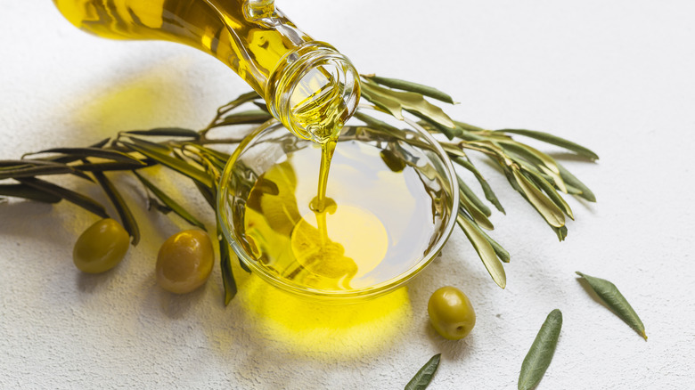 Olive oil being poured into bowl, with olives around it