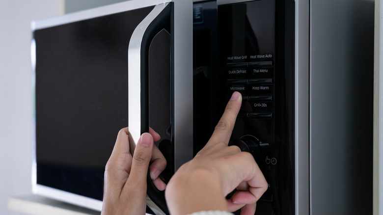 fingers pushing microwave buttons