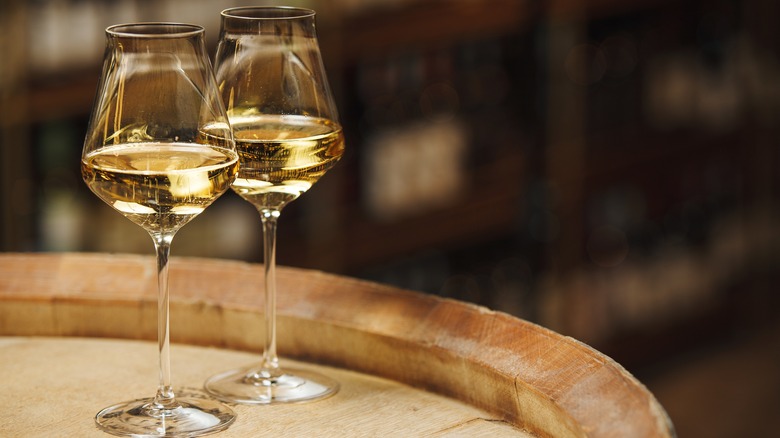 Two glasses of white wine sitting on top of an oak barrel