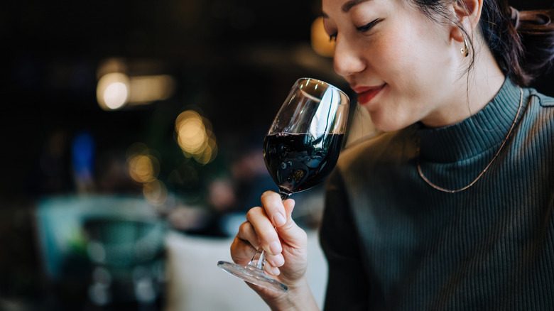 A young woman holds a glass of red wine up to her nose in a restaurant