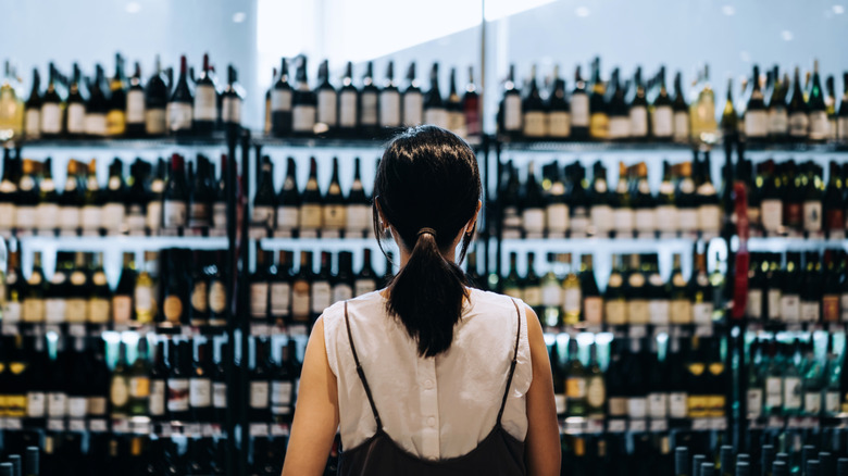 Woman stands in front of racks of wine in a supermarket