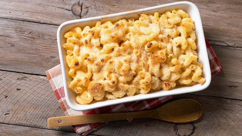 white baking sheet full of macaroni and cheese with breadcrumbs sitting on top of a red gingham towel on a wooden table.
