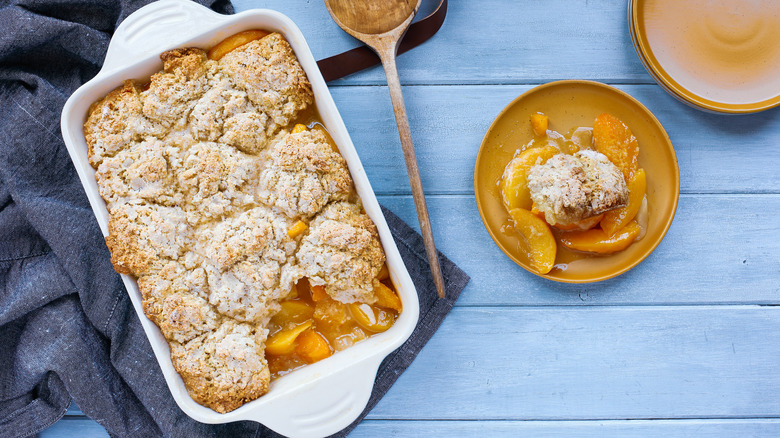 a baking sheet with drop biscuit peach cobbler next to a plate with a serving of cobbler on it.