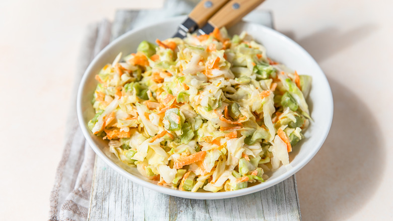 a bowl of coleslaw on a wooden board against a white background.
