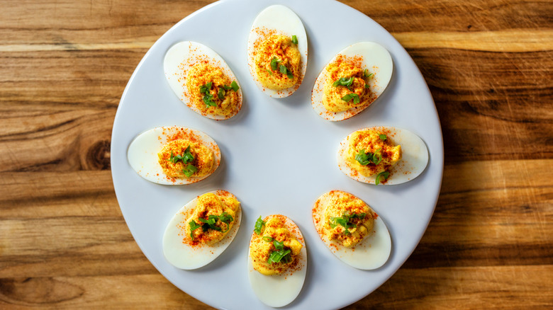 a plate of deviled eggs arranged in a circle on a white plate on a wooden table.