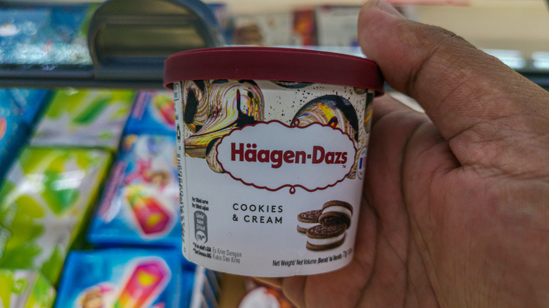 A hand holds a carton of Häagen-Dasz cookies and cream ice cream
