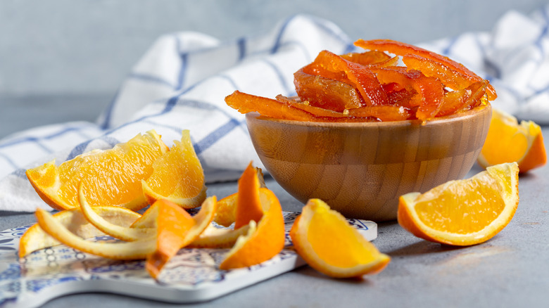 Candied orange peels in a bowl with fresh oranges and orange pees on the side on a table