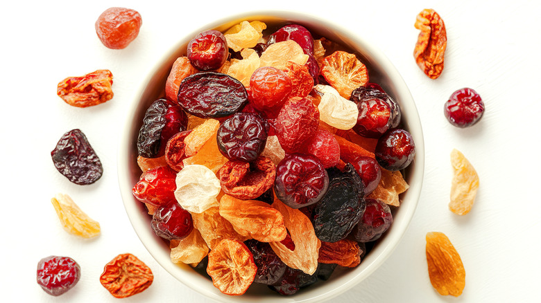 A bowl full of dried fruits with some on the side on a white table