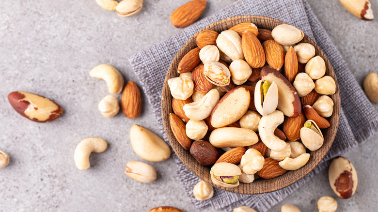 A bowl of mixed nuts on a table with some nuts scatterd on the side