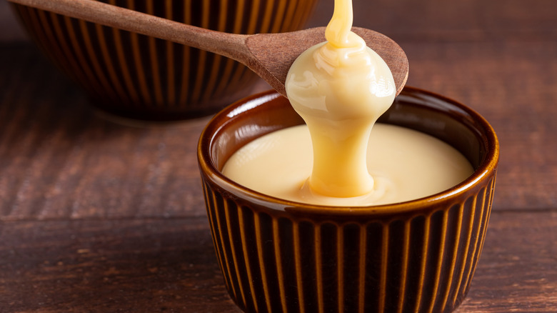 Fresh condensed milk pouring over a wooden spoon into a bowl