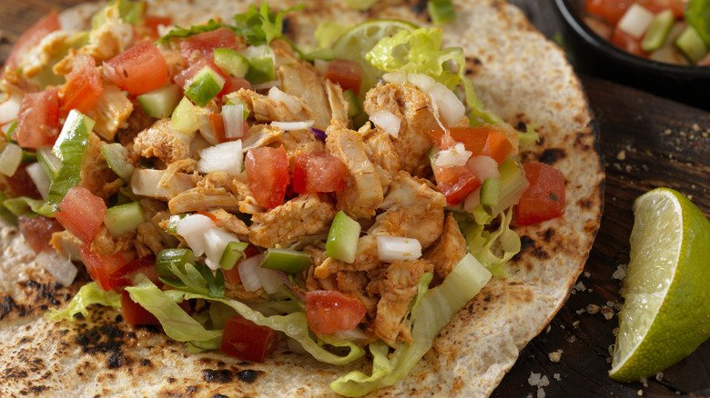 Unfolded chicken taco, topped with diced tomatoes and onions