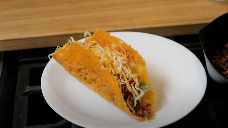 A taco with a cheese shell sits on a white plate