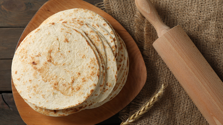 A stack of homemade tortillas next to a rolling pin