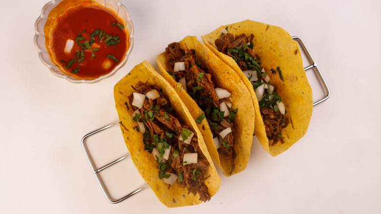 Row of birria tacos with a bowl of sauce