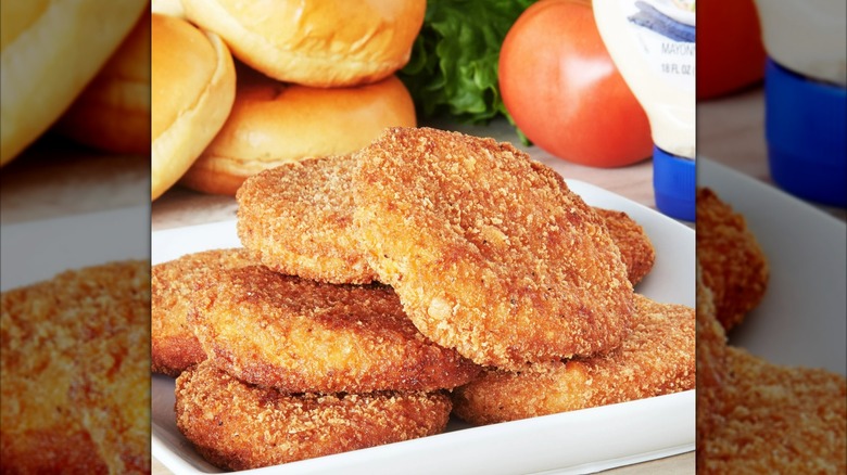 Breaded chicken breast patties on a white plate with buns in the background