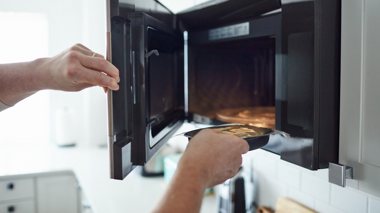 person putting frozen dinner in microwave