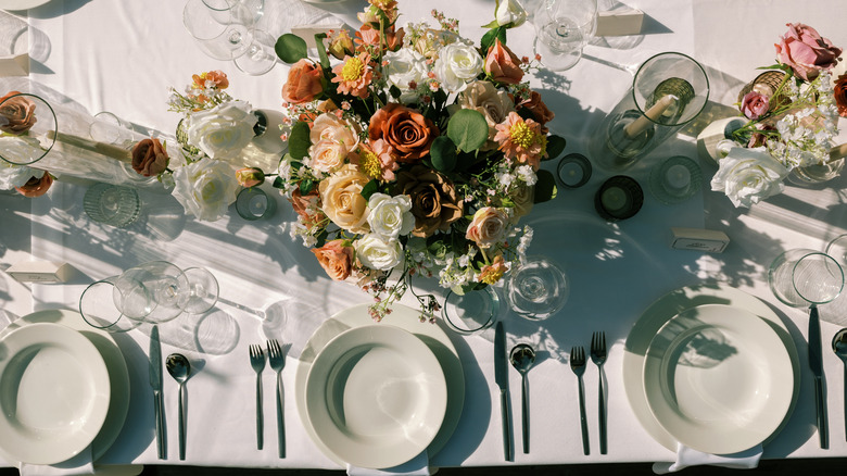 An array of flowers and white plates adorn a white tablecloth