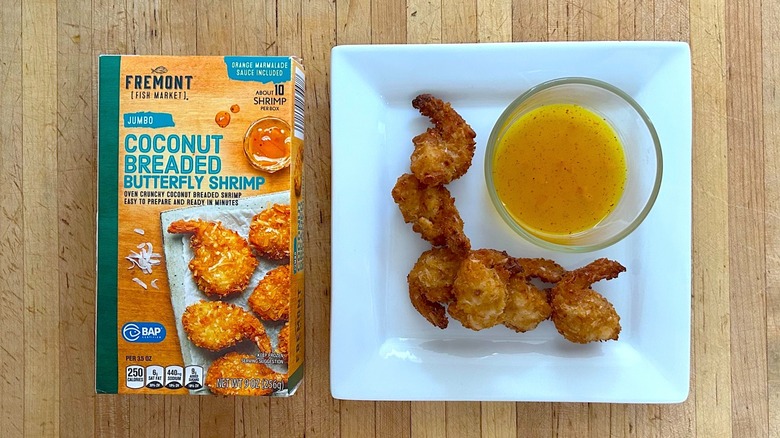 Box and white plate of Fremont Fish Market Jumbo Coconut Breaded Butterfly Shrimp with Orange Marmalade Sauce in small glass bowl